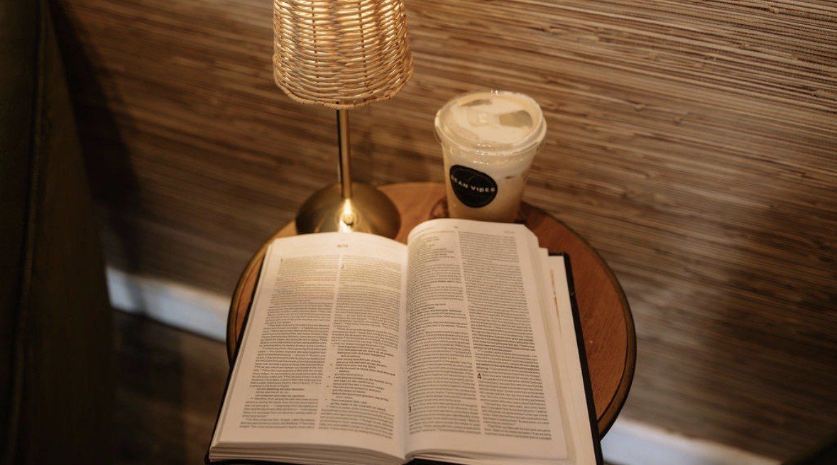 An open Bible beside a coffee under the lamp
